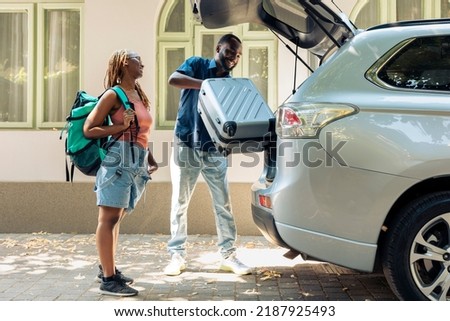 African american partners travelling by vehicle, putting luggage and baggage in trunk to leave on summer holiday. People in relationship going on vacation trip with trolley and travel bags. Royalty-Free Stock Photo #2187925493