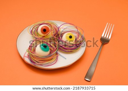 Colorful eyeball Halloween candies and spagetty on a white plate against vivid orange background. Spooky concept.