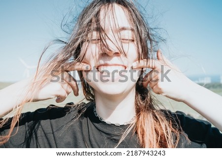 Young happy fun carefree girl smiling with big teeth to camera while pointing her dimples to camera. Bright and great future concept. Sustainable world, new generations, gen z world. Modern look. Royalty-Free Stock Photo #2187943243