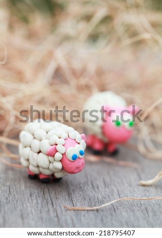 Plasticine world - little homemade white sheep stand on a farm on background of hay, selective focus on the first