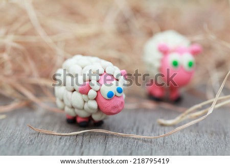Plasticine world - little homemade white sheep stand on a farm on background of hay, selective focus on the first 
