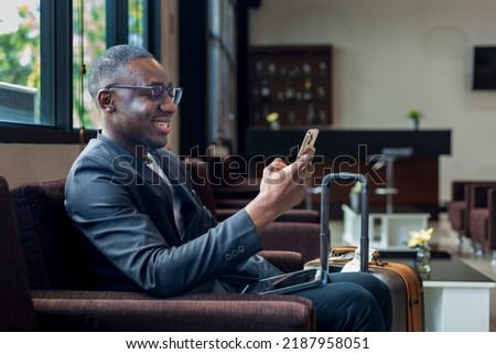 African American businessman is using mobile phone for video call while waiting in airline business departure lounge waiting for boarding airplane Royalty-Free Stock Photo #2187958051