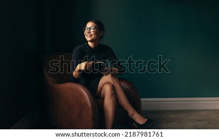 Happy businesswoman sitting on armchair with cup of tea. Beautiful woman relaxing on armchair and looking away. Royalty-Free Stock Photo #2187981761