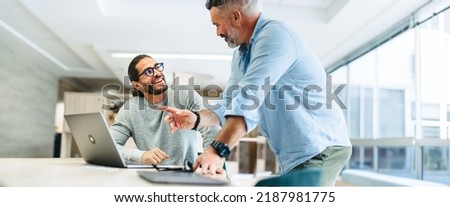 Successful businessmen smiling happily while working together in a co-working office. Two cheerful businessmen using a laptop while working on a new project. Royalty-Free Stock Photo #2187981775