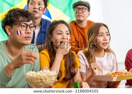 Group of Asian man and woman friends watching soccer games national competition on television with eating snack together at home. Sport fans people shouting and celebrating sport team victory match.