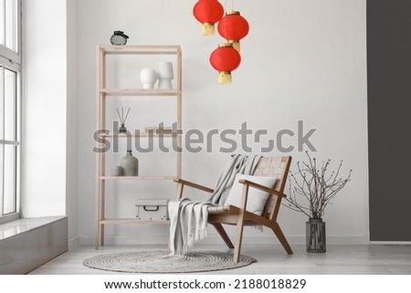 Interior of light living room with shelving unit, armchair and Chinese lanterns Royalty-Free Stock Photo #2188018829