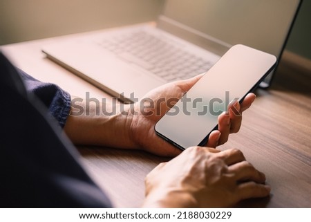 Mockup image of a man holding and using smartphone with blank desktop screen while working and drinking coffee in cafe.