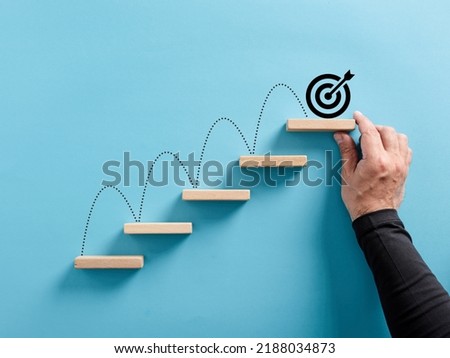 Male hand arranges a wooden block staircase with target icon. Achieving goals and objectives or goal setting concept. Royalty-Free Stock Photo #2188034873