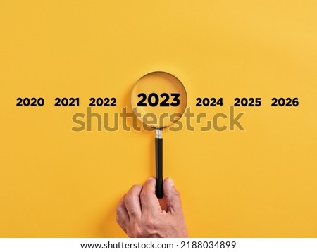 Male hand holds a magnifier focusing on the year 2023. Focus on new business goals, plan and strategy of the year 2023 concept.