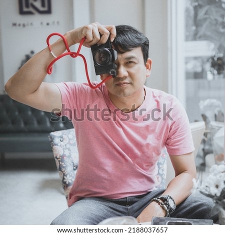 Hipster young man with analog vintage photo camera makes photograph into lens in cafe, Thailand.