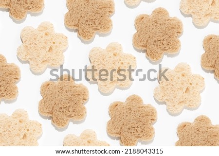 Flower shaped cut-outs from slices of white and whole-grain brown toast bread on isolated pastel white background. Minimal flat lay texture. Food comparison idea. Top view. Creative abstract pattern.