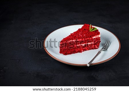 A piece of red velvet cake with mascarpone cream cheese filling, garnished with mint, served on a blue plate with a dessert fork, dark background