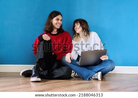 Couple of teenage students using laptop sitting on the floor on blue background