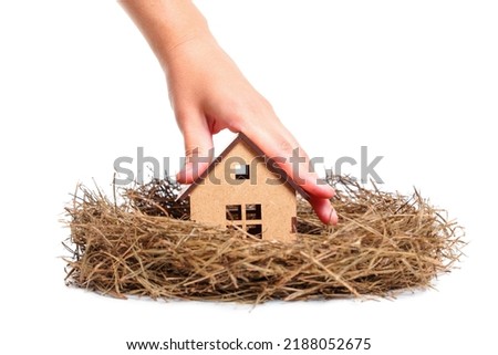 Hand placing a miniature wooden house in a hay nest isolated on white background. Family house concept.