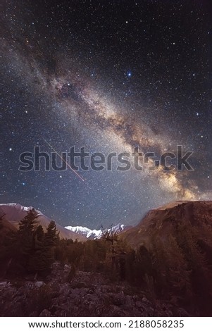 Starry sky and milky way over mountains. Flying meteor. Super wide angle. A large number of small stars throughout the image field. Soft focus on the stars.