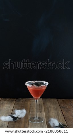 Scary red cocktail with spider on black background and wooden table for Halloween. Vertical photo. Copy space.