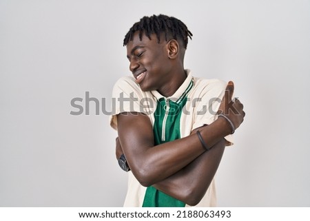 African man with dreadlocks standing over isolated background hugging oneself happy and positive, smiling confident. self love and self care 