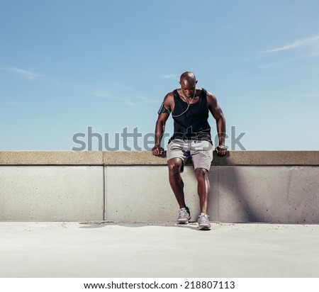 Muscular young man taking breath after his run. African male athlete outdoors with copy space. Male runner relaxing after running exercise.