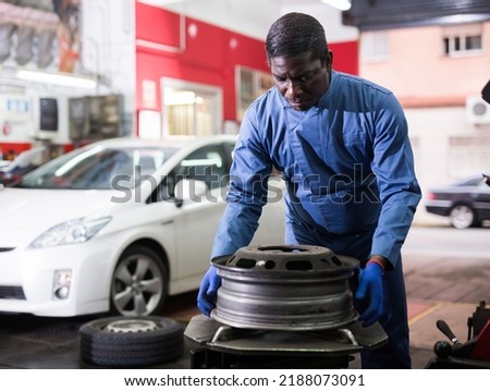 Afro american man working with tire fitting machine at auto car repair service center
