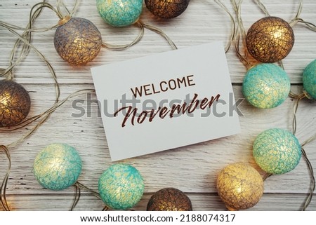 Welcome November text on paper card with LED cotton balls top view on wooden background