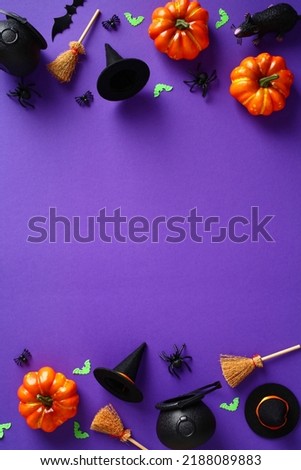 Happy Halloween holiday concept. Halloween decorations, pumpkins, bats, witch hats, brooms on purple background. Halloween party greeting card mockup with copy space. Flat lay, top view, overhead.