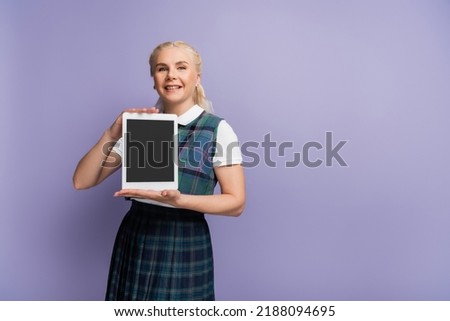 Cheerful blonde student holding digital tablet with blank screen isolated on purple