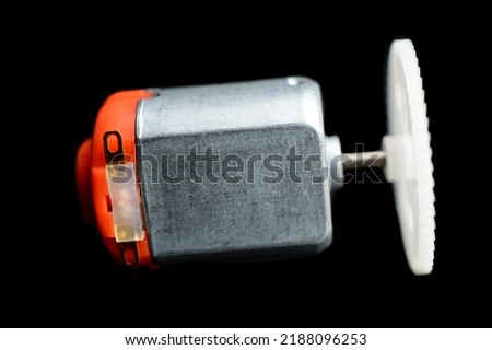 Direct current electric motor with white gear attached to it shaft on a black background. Macro photo. Background picture.