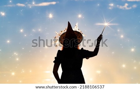 Black silhouette of witch with magic wand isolated on fairy star sky background.Beautiful young woman in black robe and wizard hat conjuring, making witchcraft. Halloween party art design.Copy space 