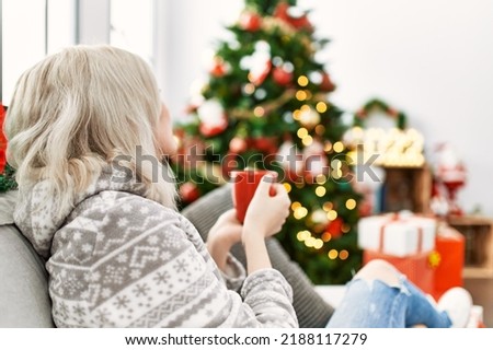 Young caucasian girl sitting on the sofa drinking coffee celebrating christmas at home.