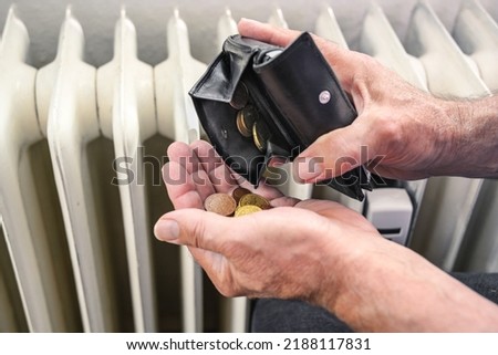 Hands of a man pouring out few coins from a wallet in front of an old heater, suffering from rising energy costs, copy space, selected focus, narrow depth of field Royalty-Free Stock Photo #2188117831