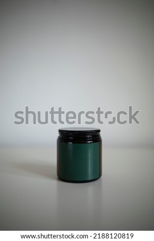 dark glass jar with a dark green empty label on a white background. closed jar with a candle close-up.