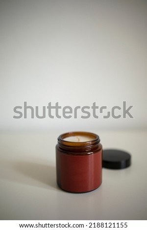 dark glass jar with a dark red or burgundy empty label on a white background. open jar with a candle close-up.
