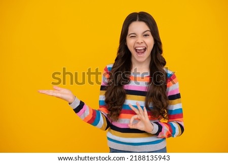 Amazed teenager. Portrait of cute teenager child girl pointing hand showing adverts with copy space over yellow background. Excited teen girl.