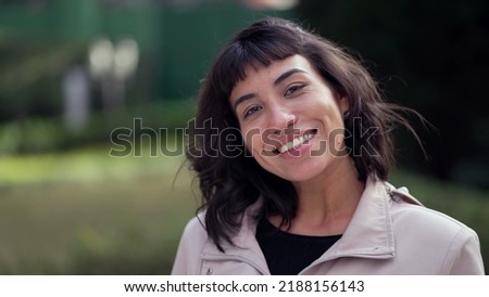 Happy South American young woman portrait face smiling at camera standing outside. Young latin person in 20s. Tracking shot in motion