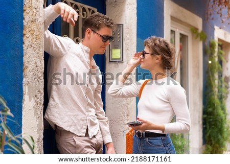 Smiling beautiful woman and her handsome boyfriend. Woman in casual summer jeans. Man standing near door woman flirting with handsome guy holding phone in hand Royalty-Free Stock Photo #2188171161