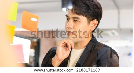 Thinking businessman writing on colorful notes attached to a glass wall the entrepreneur creates planning visual list.