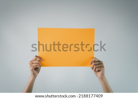Mock Up Template photo concept.,Hand Holding Blank Orange paper for banner,advertising isolated over white wall background.