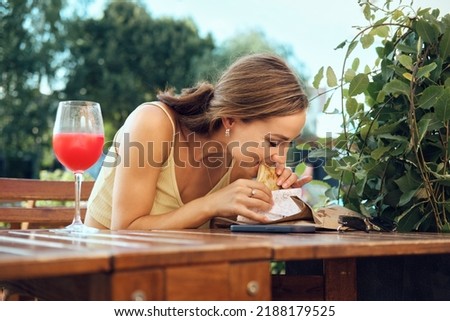 Young woman bites slapjack stuffed with bacon, ham and cheese sitting at outdoor terrace Royalty-Free Stock Photo #2188179525