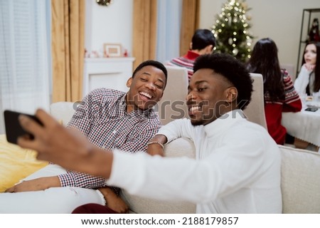 The day of Christmas Eve Day the family has dinner together, two brothers sit on the couch and take a souvenir photo, selfie with a smartphone with a smile, joy