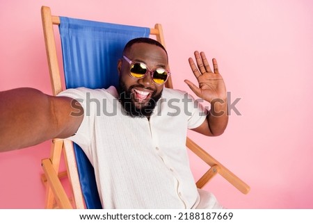 Photo of excited pretty guy dressed white shirt sitting deck chair recording self video waving arm isolated pink color background