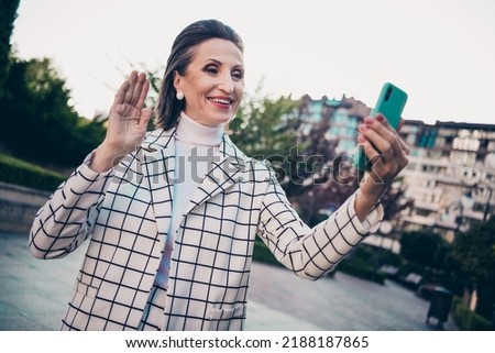 Photo of funny friendly woman wear plaid jacket tacking selfie modern device waving arm outside city residential complex