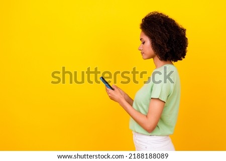 Photo of confident pretty girl dressed green t-shirt chatting modern device empty space isolated yellow color background