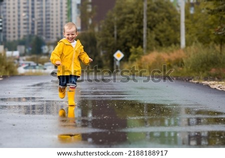 A small child in rainbow socks, yellow rubber boots and a jacket runs through puddles, has fun and plays after the rain. A picture of summer and autumn holidays. A happy child.