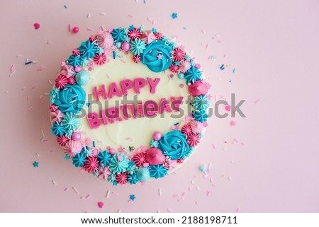 Birthday cake with colorful happy birthday greeting and sprinkles on a pink background, overhead view