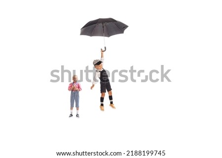 Portrait of two playful boys, children in jumpsuit posing isolated on white studio background. Flying with umbrella. Fairy tail. Concept of childhood, friendship, fun, lifestyle, fashion. Retro style