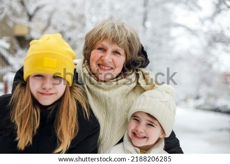 Joyful family grandmother with grandchildren in warm clothes playing outdoors in winter park, enjoying frosty and snowy weather, children actively spending new year holidays in fresh air with grandma