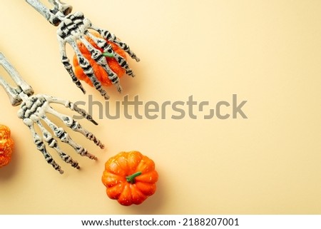 Halloween decorations concept. Top view photo of pumpkins and skeleton hands on isolated beige background with copyspace