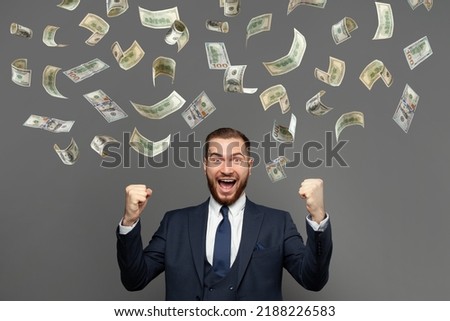 Excited happy successful man standing under money rain against gray background