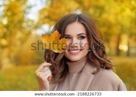 Closeup portrait of a beautiful autumn woman standing near colorful autumn leaves. Pretty happy cheerful model looking at camera.