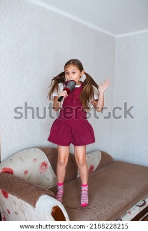 Beautiful brunette little girl singing in brush at home. Kid enjoying singing hairbrush mic. Recording studio.